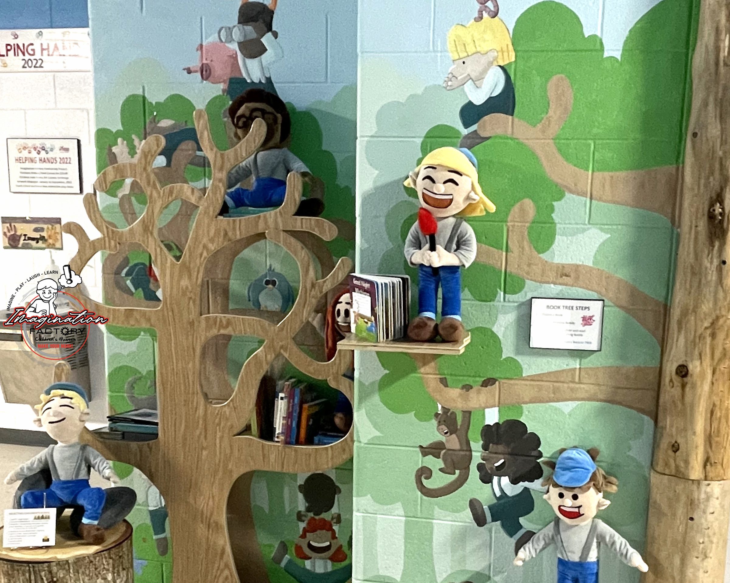 Children play on a colorful indoor playground with tree and character murals.