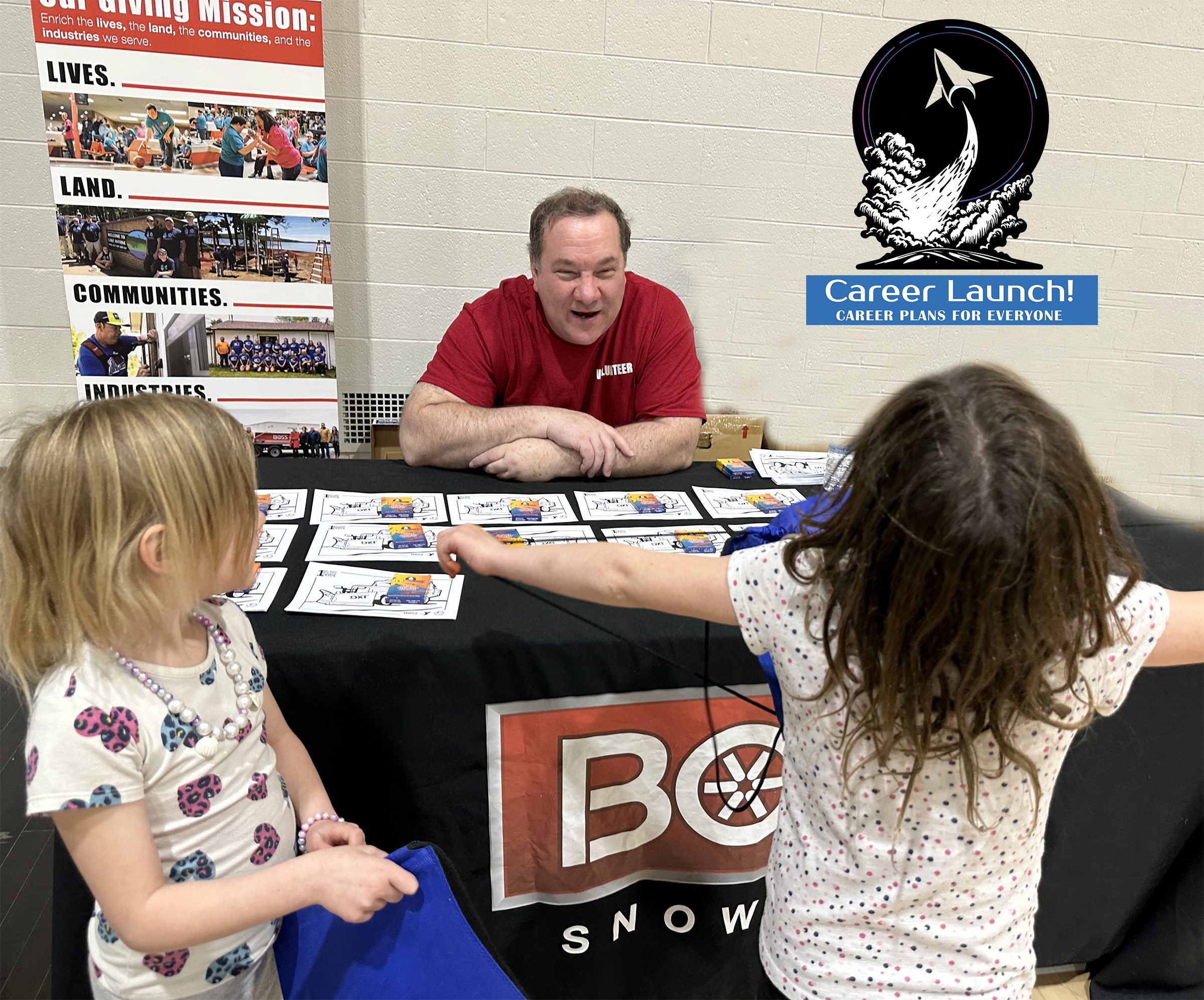 A man at a booth interacting with two children at an event.