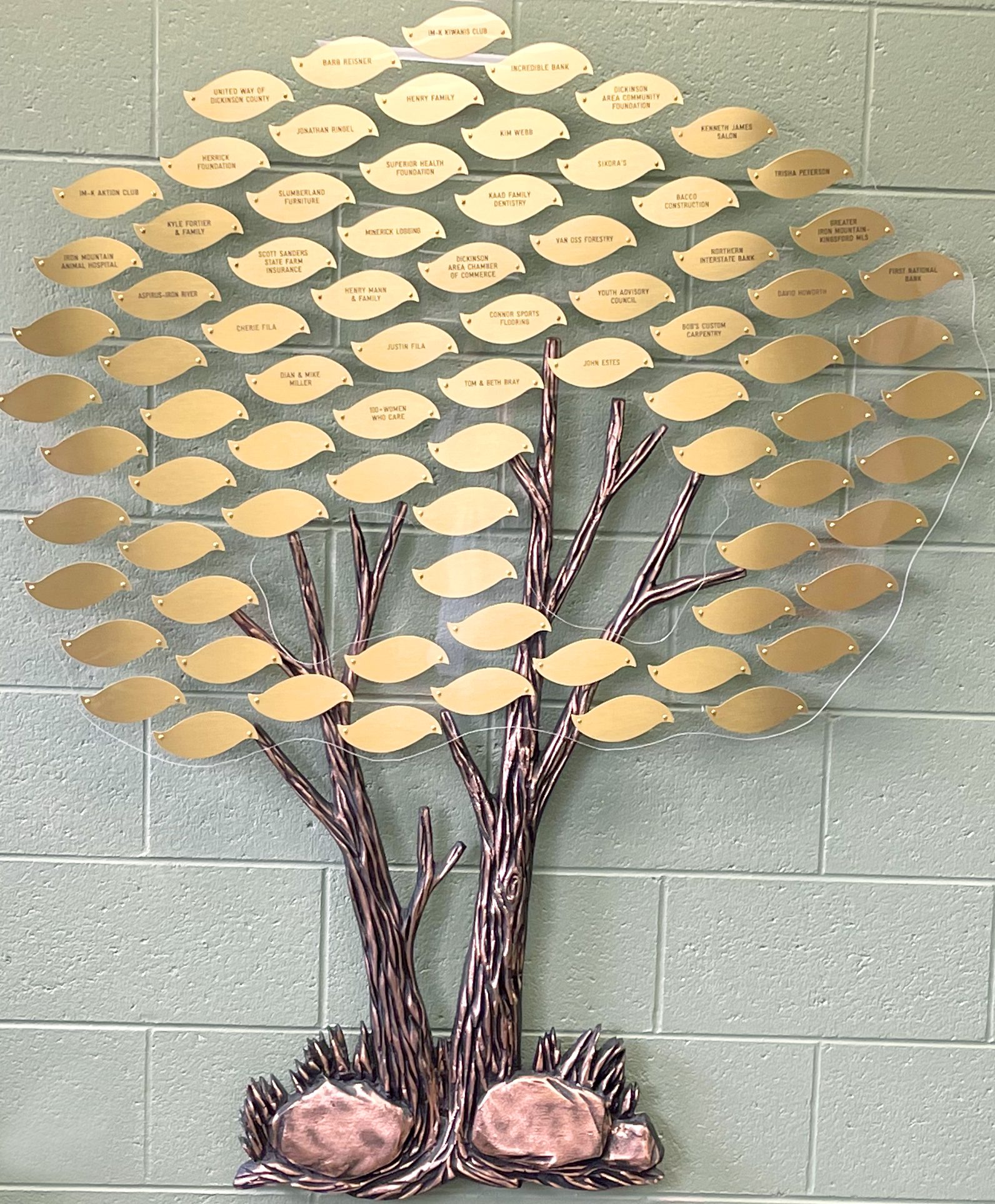Artistic tree sculpture with wooden leaves mounted on a gray wall.