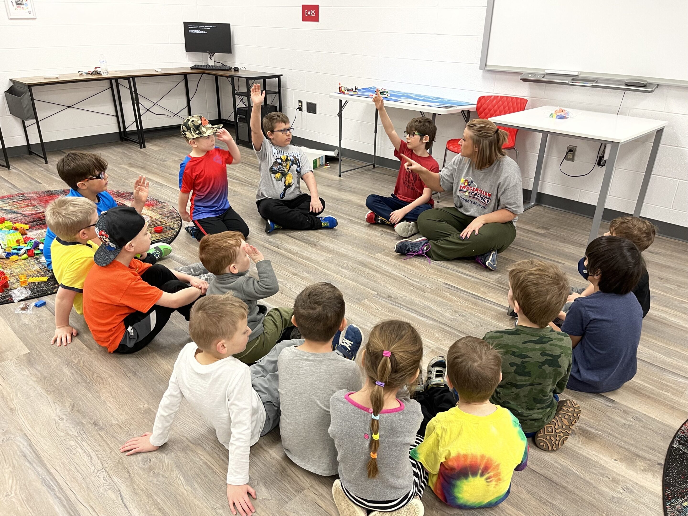 Children sitting in a circle listening to a teacher in a classroom.