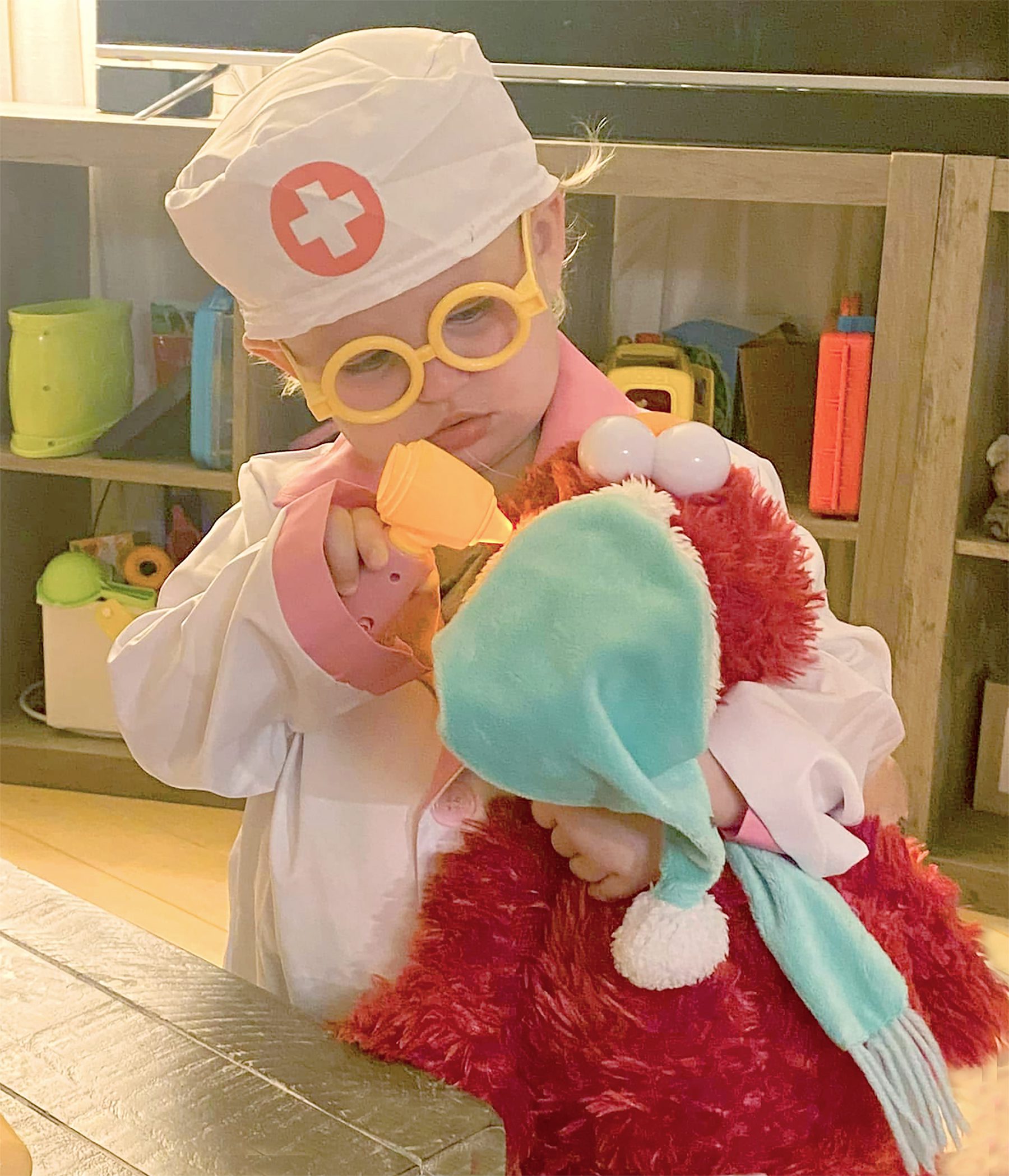 Child dressed as a nurse playing with a stuffed Santa Claus toy.
