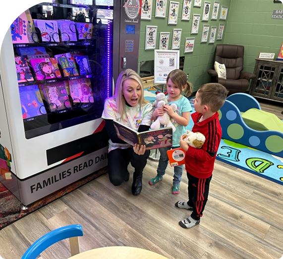A woman reads a book to four young children in a colorful classroom.