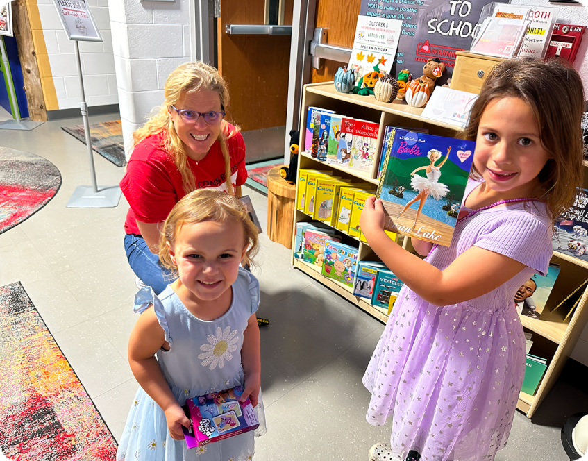 Three children happily holding books in a colorful bookstore section.