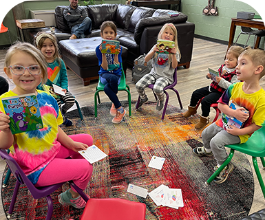 Children sitting in a circle playing a card game indoors.