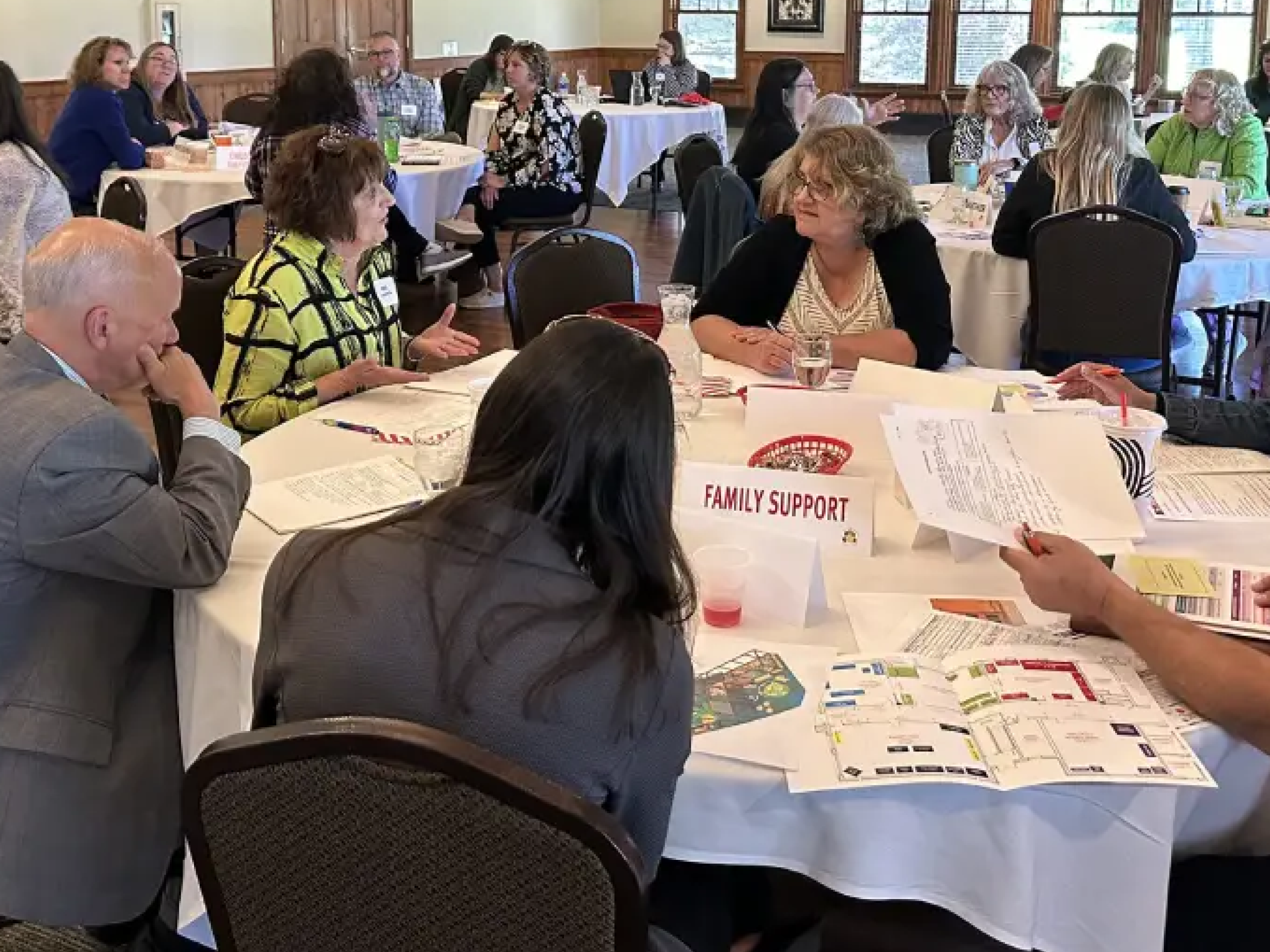 People engaged in discussions around a conference table with documents and name tags.