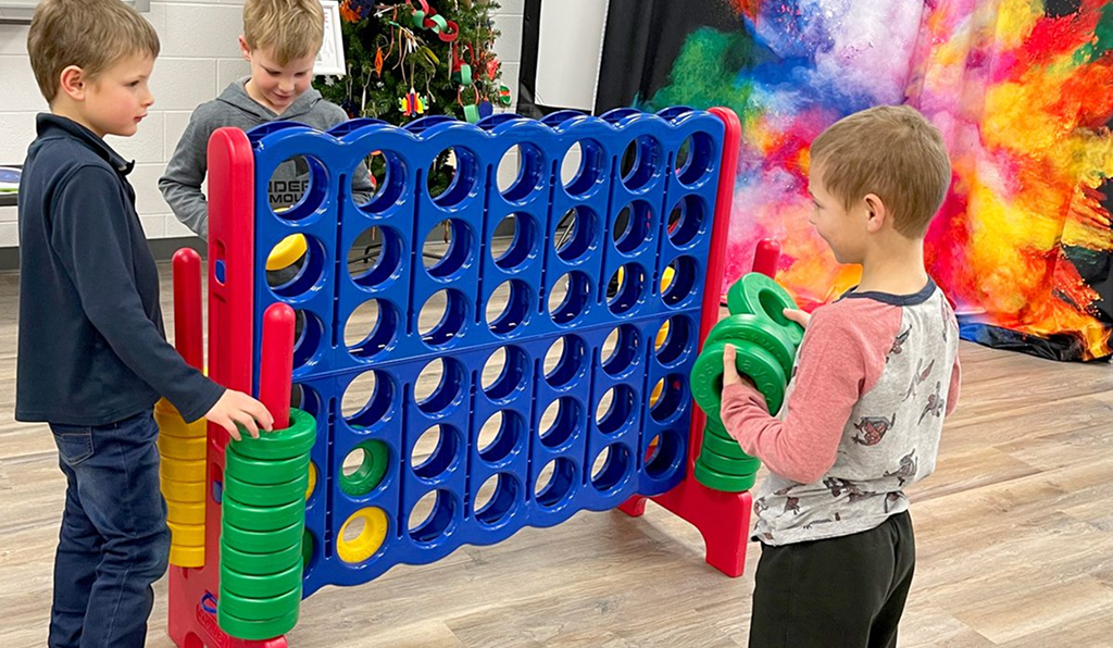 Two children playing a giant Connect 4 game indoors.