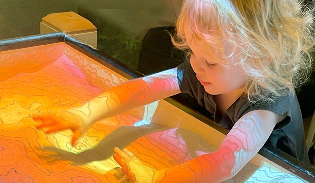 A child playing with colorful light projections on a table.