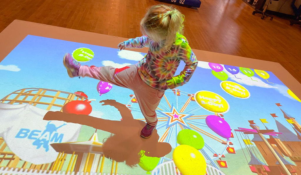 Child joyfully playing on an interactive colorful floor projection.