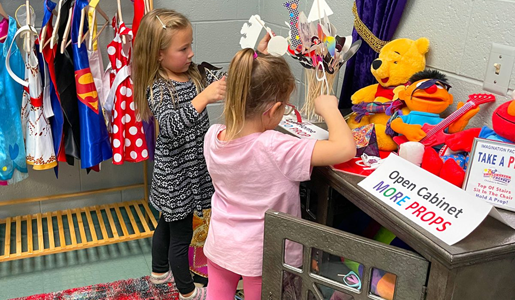 Two young girls playing with puppets in a colorful room.