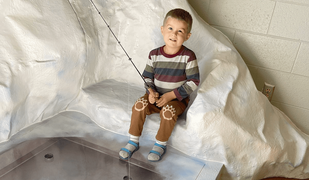 A young boy sitting on a white textured surface, smiling gently.