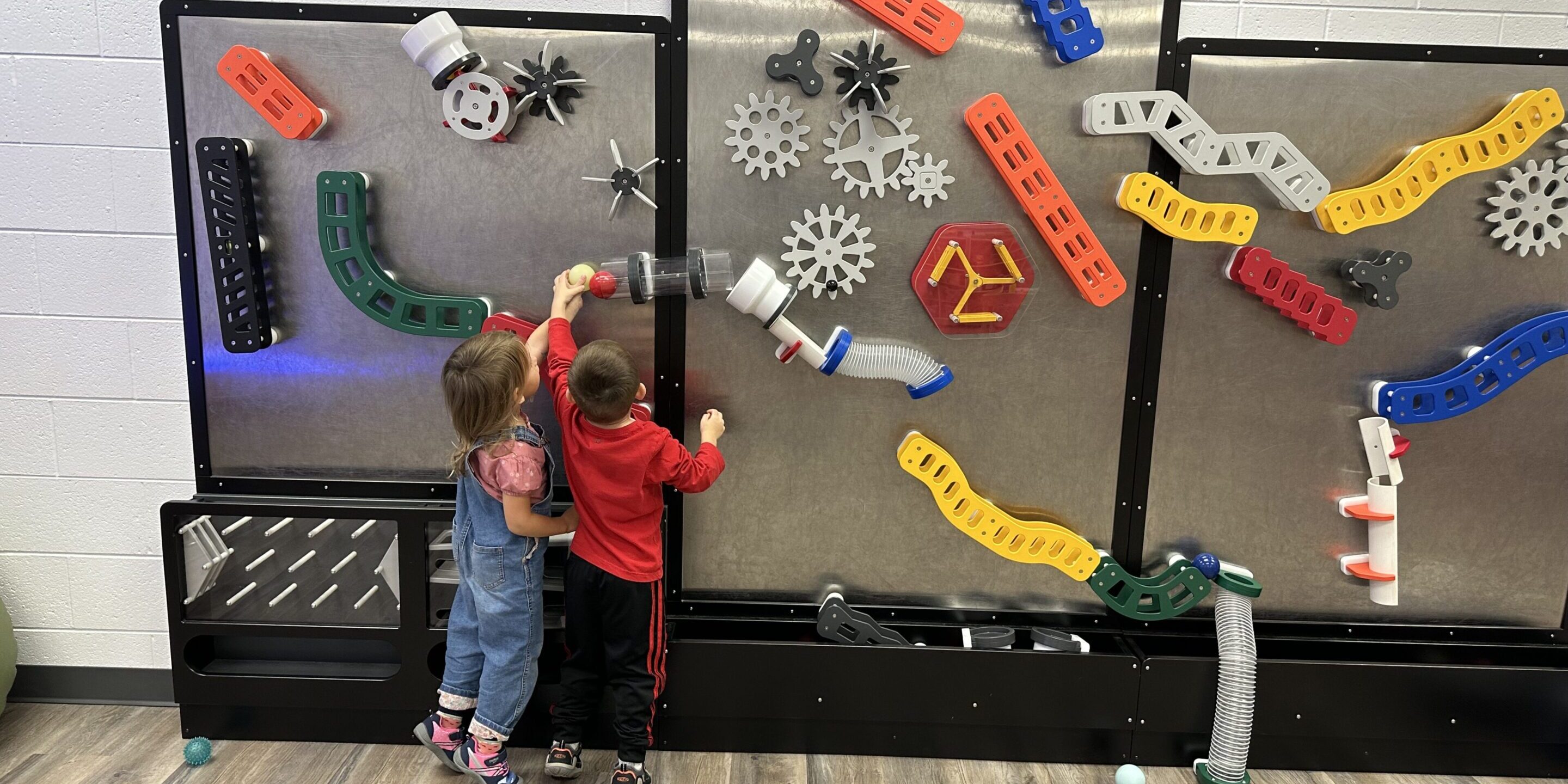Two children playing with a colorful marble run wall toy.